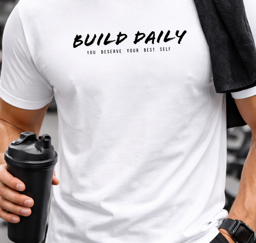 Person wearing a white t-shirt with 'Build Daily' text, holding a black shaker bottle.
